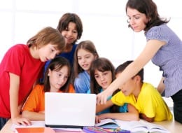Teacher instructing elementary schoolchildren on using the laptop computer