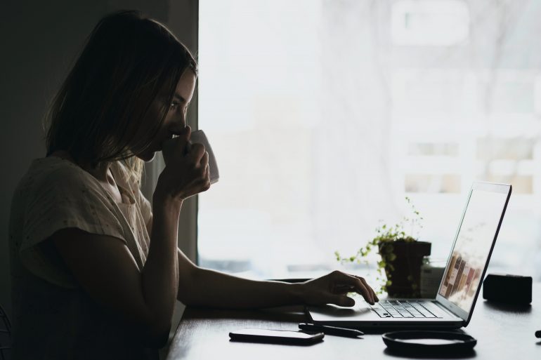 Foto van een vrouw aan een bureau met een laptop, smartphone en kop koffie