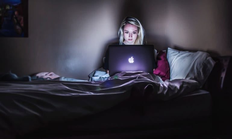Vrouw zit in het donker met macbook in bed. 
