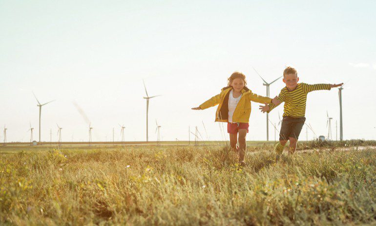 Kinderen rennen over een grasveld, op de achtergrond moderne windmolens. 
