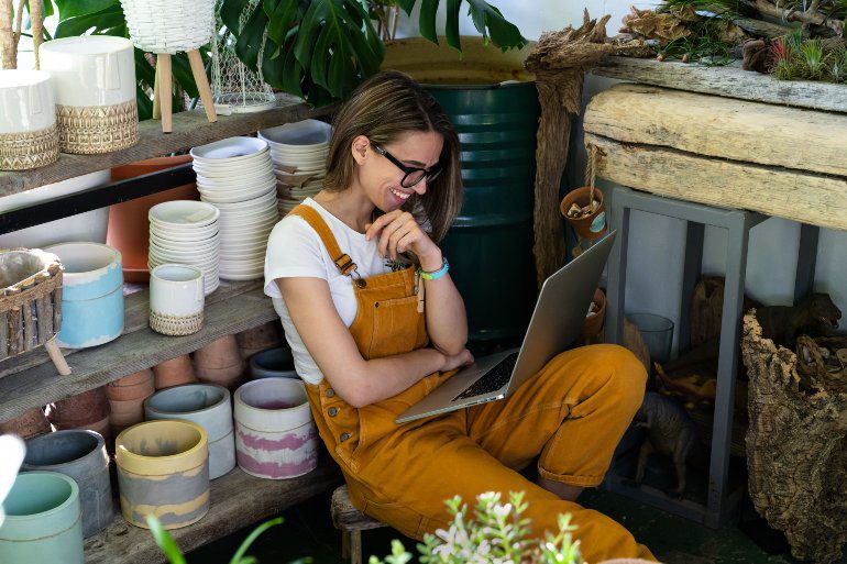 Vrouw in bloemenwinkel werkt aan contentmarketing op laptop.