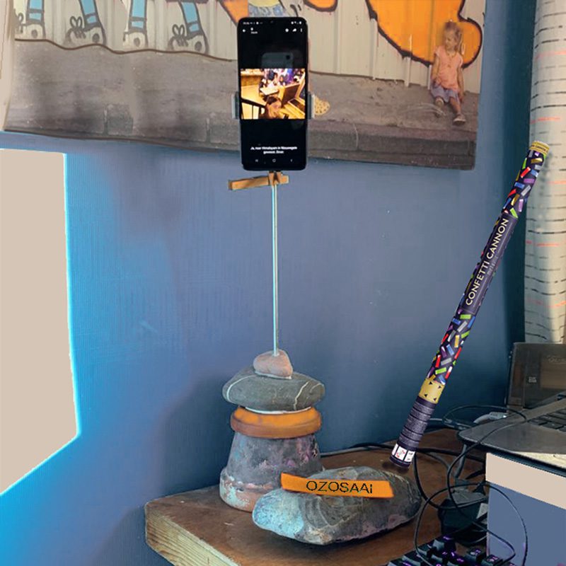 Mobiele telefoon op een staander naast het pc scherm en in de hoek een confettikanon