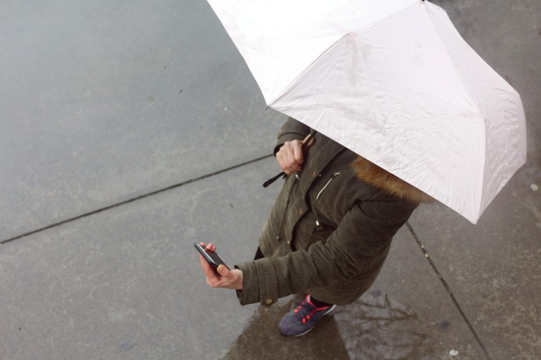 Mens onder paraplu kijkt op mobiele telefoon.
