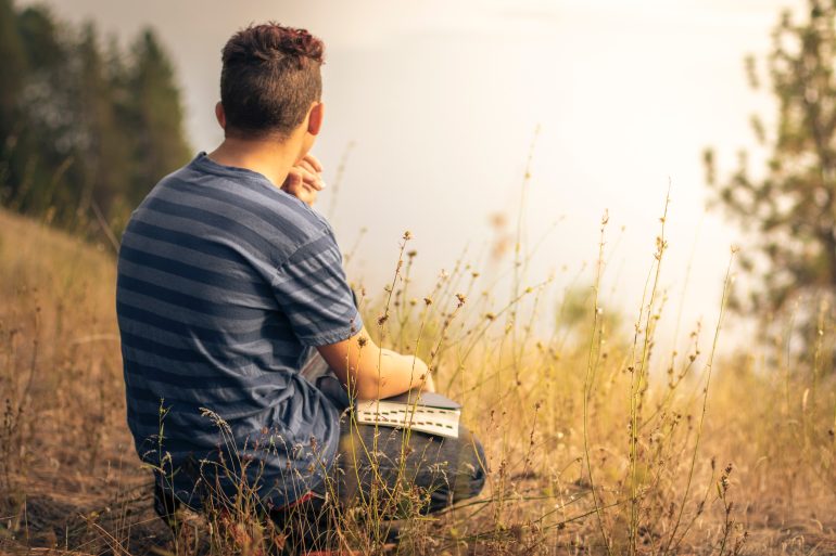 Foto van een man die in een veld zit met een gesloten boek op schoot | Bron: Unsplash