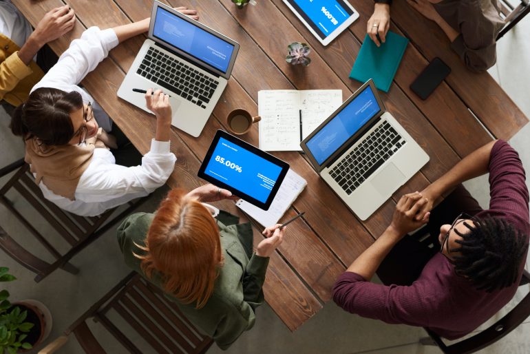 groep mensen van bovenaf gefotografeerd aan een tafel met laptops erop